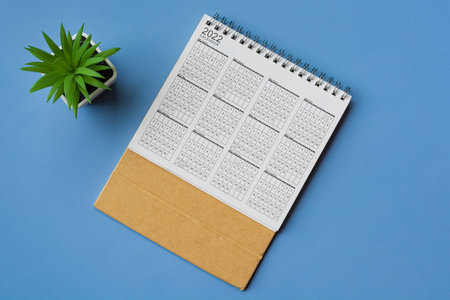 2022 white calendar with potted plant on blue background. Directly above. Flat lay. Resolution and...