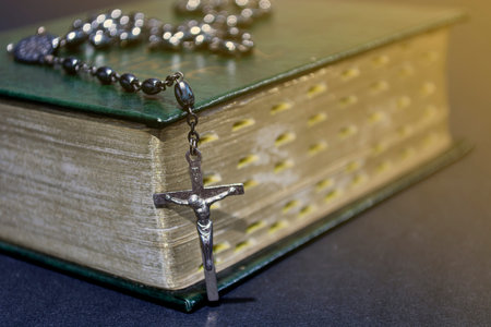 The cross over bible on wooden table with window light, vintage tone and dark background. Religion...