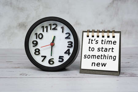 Motivation text on notepad with black alarm clock set time at 12.30 on wooden desk - It is time to start something new.の写真素材