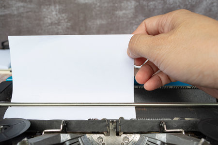 Hand pulling a piece of white paper from an old classic typewriter on wooden desk. Copy space. For text purpose.の写真素材