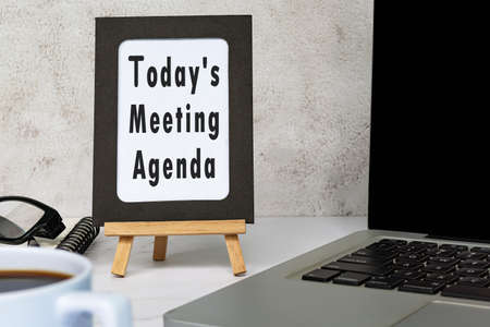 Today's meeting agenda text written on chalkboard with notebook on white desk. Meeting and goal concept.の写真素材