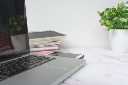 Laptop on white table with potted plant, notebooks and smartphone.の写真素材