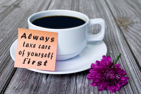 Text written on stick note with white coffee cup and purple flower on wooden desk - Always take care...