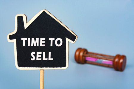 Text on wooden house with background of hourglass. Time to sell real estate concept. Copy space.