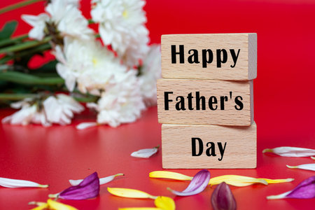 Text on wooden cube and with flower on red background - Happy Father's Day. Event and celebrations.