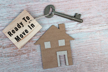 Ready to move in text on wooden keychain with house model and key on wooden desk. Real property...