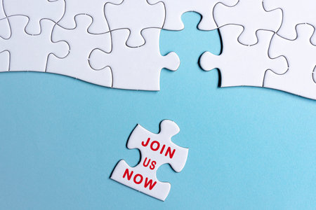 White jigsaw puzzle with word join us now over blue background. Recruitment and job vacancy concept.