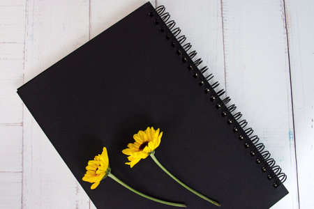 Black note book flat lay with sunflowers on wooden desk. Directly above.の写真素材