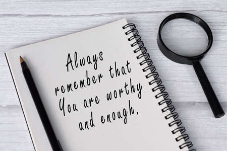 Motivational quote on note book with magnifying glass on white wooden desk.の写真素材