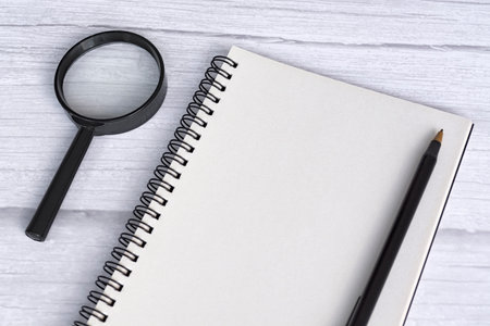 Note book flat lay with magnifying glass on white wooden desk. Directly above