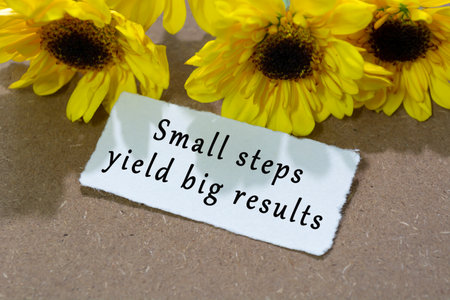 Motivational quote on torn white paper with sunflower on wooden table background - Small steps yield big resultsの写真素材