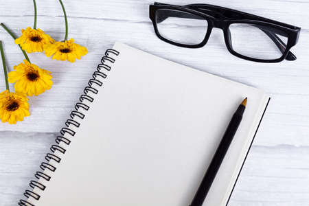 Notepad flat lay with sunflowers, reading glasses and pen on wooden desk. Directly above. Copy space.の写真素材