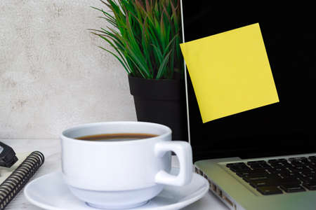Sticky note on a notebook or laptop black screen with other accessories and coffee on white table.の写真素材