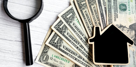Wooden house model with dollar banknotes and magnifying glass on wooden table. Concept for real...