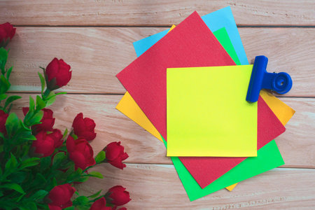 Colorful note flat lay with artificial flower on wooden background. Directly above. Copy space.