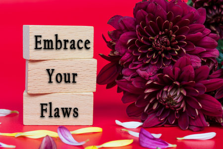 Embrace your flaws text on wooden cube and with flowers bouquet on red background.