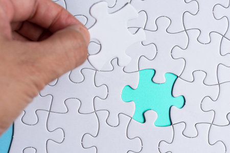 Person's Hand Holding Piece Of Puzzle With Green Background. Copy Space.