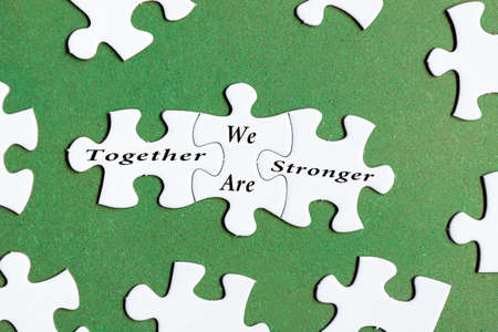 Motivational text on white jigsaw puzzle with green background - Together we are stronger.の写真素材