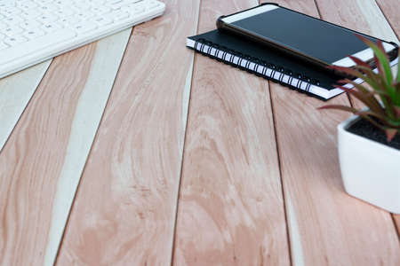 Cellphone, note book, potted plant and white keyboard on wooden desk. Copy space.の写真素材