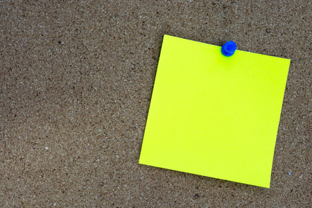 Yellow stick note and pinned to a cork notice board. Copy space. Reminder concept.の写真素材