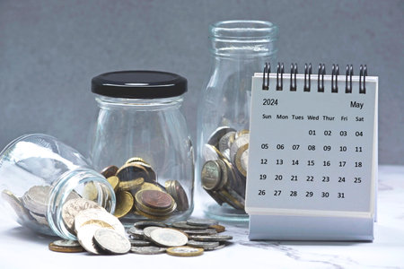 May 2024 calendar and glass jars with multicurrency coins. 2024 finance concept.の写真素材