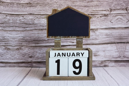 Chalkboard with January 19 date on white cube block on wooden table.の写真素材