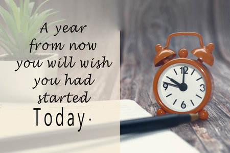 Motivational quote with alarm clock on wooden background - A year from now you will wish you had started today.の写真素材