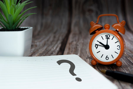 Question mark on notepad alarm clock set at 10 o'clock on wooden background. Q & A concept.の写真素材