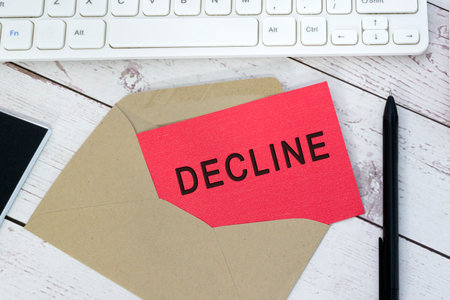 Decline text on red card with envelope, white keyboard and pen on wooden table. Communication concept.の写真素材