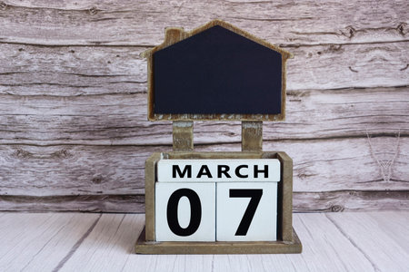 Chalkboard with March 07 calendar date on white cube block on wooden table.の写真素材