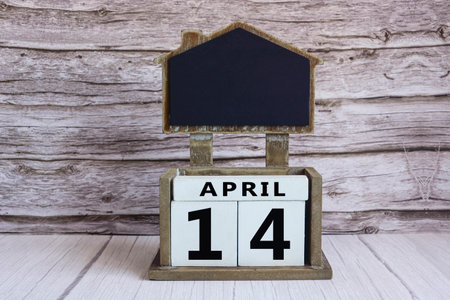 Chalkboard with April 14 date on white cube block on wooden table.の写真素材