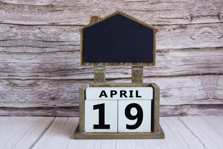 Chalkboard with April 19 date on white cube block on wooden table.の写真素材