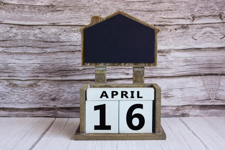 Chalkboard with April 16 date on white cube block on wooden table.の写真素材