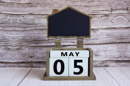 Chalkboard with May 05 date on white cube block on wooden table.の写真素材
