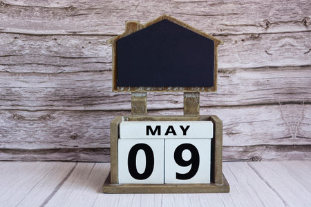 Chalkboard with May 09 date on white cube block on wooden table.の写真素材