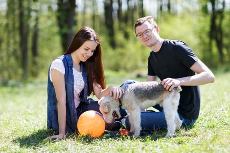 Young couple hugging their little dog sitting in summer parkの写真素材