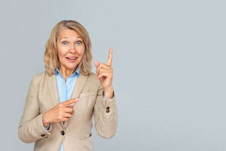 Portrait of business woman pointing up and looking at the camera over gray backgroundの写真素材
