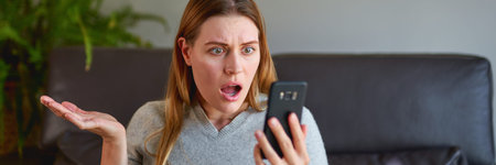 Unhappy woman sitting on sofa with laptop and talking on phone at home.