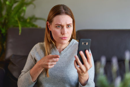 Sad woman sitting on sofa with laptop and talking on phone at home. College student studying on...