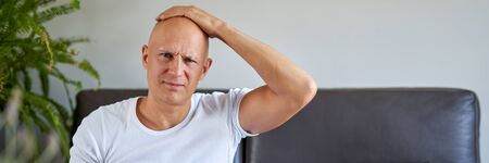 Feeling depressed. Desperate young man keeping his hand on forehead while sitting on the couch at homeの写真素材