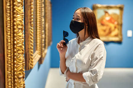 woman visitor wearing an antivirus mask in the historical museum looking at picturesの写真素材