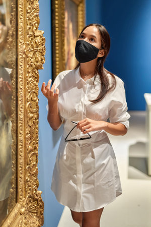 girl visitor wearing an antivirus mask standing near pictures in museum of arts