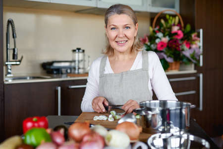 Senior woman in the kitchen cooking, mixing food in a potの写真素材