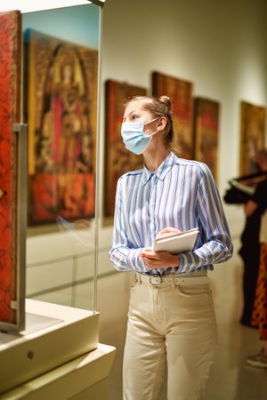 Woman visitor wearing an antivirus mask in the historical museum looking at pictures.の写真素材