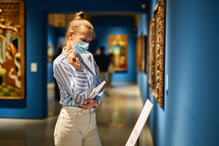 Woman visitor wearing an antivirus mask in the historical museum looking at pictures.