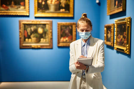 Woman visitor wearing an antivirus mask in the historical museum looking at pictures.の写真素材