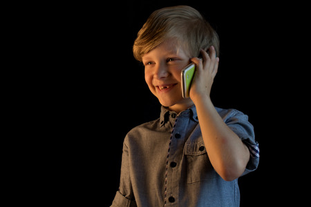 A boy is calling and talking on his mobile phone. He has a good mood, he smiles.の写真素材