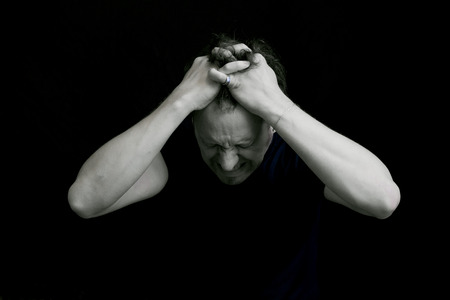 The man feels a headache. He clings to his head with his hands. A picture on a black background. Black and white photo.の写真素材