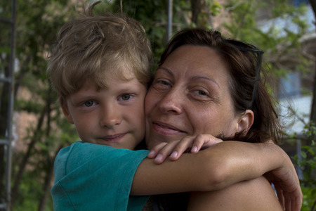 Mom and son. Son with mother in embrace. Both look into the camera, both smile.の写真素材
