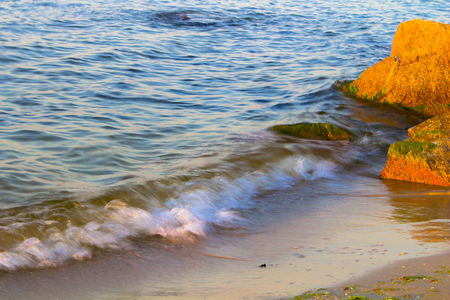 Coast of the sea, ocean. Stones on the shoreline. Blue water and orange stones at sunrise.の写真素材